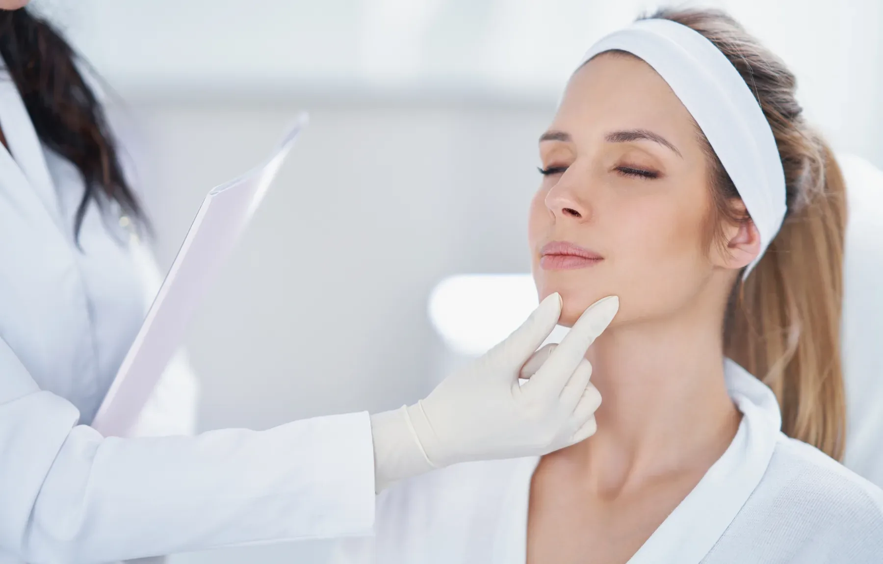 A woman with a white headband reclines with her eyes closed while a provider in a white coat holds a small pink folder in one